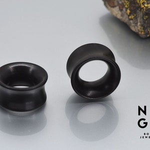May include: Two black wooden ear gauges, one is a flared style and the other is a simple ring style.