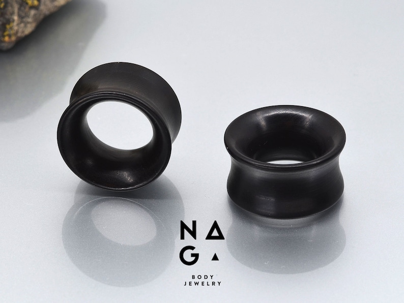 May include: Two black wooden ear gauges, one on each side of the image. The gauges are round and have a flared edge. The gauges are made of wood and have a smooth finish.
