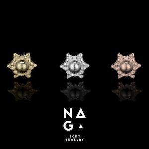 May include: Three star-shaped stud earrings in yellow gold, silver, and rose gold tones. Each earring features a central raised sphere surrounded by a textured, beaded border. The text NAGA BODY JEWELRY is printed in white below the earrings.