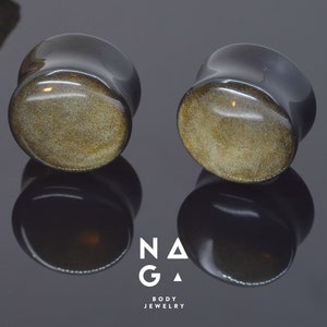 Puede incluir: Par de expansores de oreja negros y dorados con un patrón moteado.