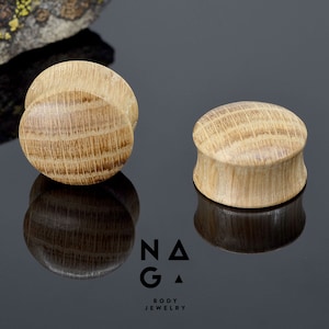 Puede incluir: Dos medidores de oreja de madera, uno en cada mano, con un patrón de veta de madera natural. Los medidores son redondos y tienen un acabado liso.