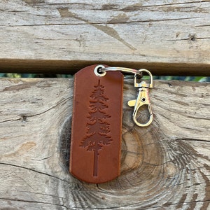 Può includere: Un portachiavi in ​​cuoio marrone con un anello portachiavi argentato e un design ad albero in rilievo sul davanti.
