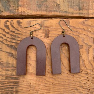 以下が含まれることがあります： アーチ型のブラウンレザーのイヤリングのペア。イヤリングはシンプルなデザインで、高品質のレザーで作られています。