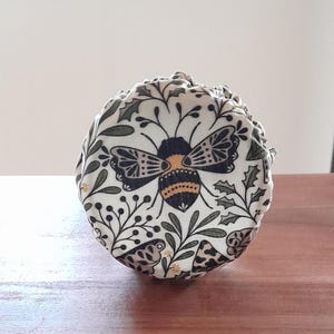 May include: A white fabric bee-themed reusable food wrap with a black and gold bee design and green foliage.
