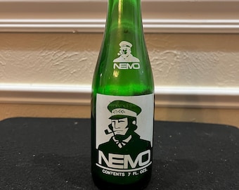 May include: A green glass bottle with a white label featuring a cartoon sailor with a pipe and the word "NEMO". The label also states "Contents 7 fl. oz."