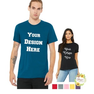 May include: Two short-sleeved t-shirts, one teal and one black, each with the text "YOUR DESIGN HERE" in white block letters. The teal shirt is modeled by a person, the black shirt by a person. A color palette is at the bottom.