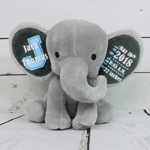 Puede incluir: Elefante de peluche gris con orejas azules y verdes. Las orejas est&aacute;n bordadas con el nombre "Jack Thomas", la fecha "16 de mayo de 2018", la hora "8:45 A.M." y el peso "7 libras 9 onzas" y la altura "22 pulgadas".