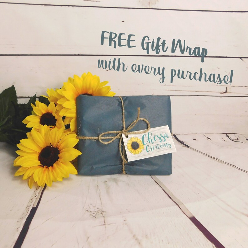 May include: A wrapped gift in teal paper tied with twine, adorned with a tag featuring a sunflower and the text "Chessa Creations." Bright yellow sunflowers with brown centers and green leaves are arranged beside the gift. The text "FREE Gift Wrap with every purchase!" is at the top.