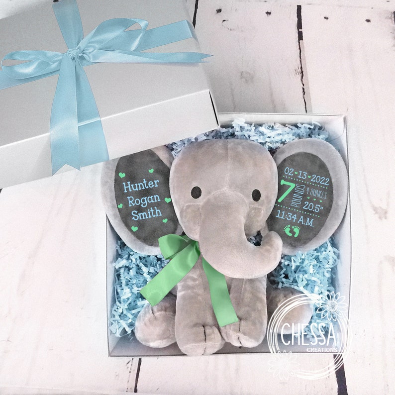 May include: A gray plush elephant baby gift set with a green ribbon. The elephant has a personalized tag with the name "Hunter Rogan Smith" and a tag with the birth details: "02-13-2022, 7 pounds 8 ounces, 20.5", 11:34 A.M."