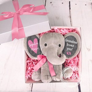 May include: A gray plush elephant toy with pink ribbon and two black felt ears. One ear has a pink heart with the text "Sophia Marie" and the other ear has the text "Grandma loves you!" with two black footprints.