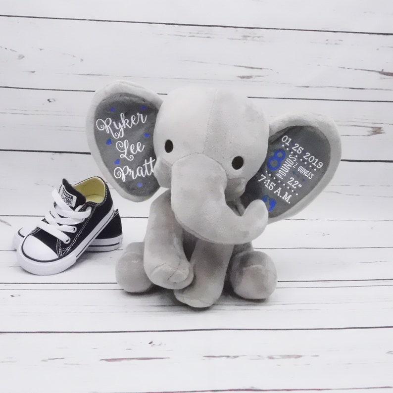 May include: Gray plush elephant stuffed animal with embroidered details. One ear says "Ryker Lee Pratt" and the other ear says "01.25.2019 8 pounds 22 ounces 7:15 A.M."