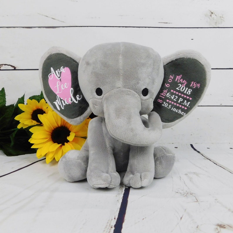 May include: Gray plush elephant stuffed animal with pink heart on one ear and embroidered text on both ears. The text on one ear reads "Ava Lee Micele" and the text on the other ear reads "8 lbs. 6 oz. May 18th, 2018 6:42 P.M. 20.5 inches".