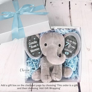 Puede incluir: Un juguete de peluche de elefante gris con detalles personalizados. El elefante est&aacute; sentado en una caja de regalo con papel de seda azul y blanco. Las orejas del elefante tienen el texto "Camila Rose Moreno" y la otra oreja tiene el texto "11-16-2019 7 pounds 12:54 PM".