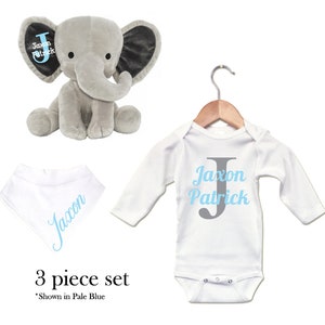 Puede incluir: Un conjunto de regalo para beb&eacute; de tres piezas con un juguete de elefante de peluche gris, un body blanco de manga larga y un babero blanco. El body y el babero est&aacute;n personalizados con el nombre "Jaxon Patrick" y la letra "J" en azul y gris. El juguete de elefante tiene la misma personalizaci&oacute;n en una oreja.