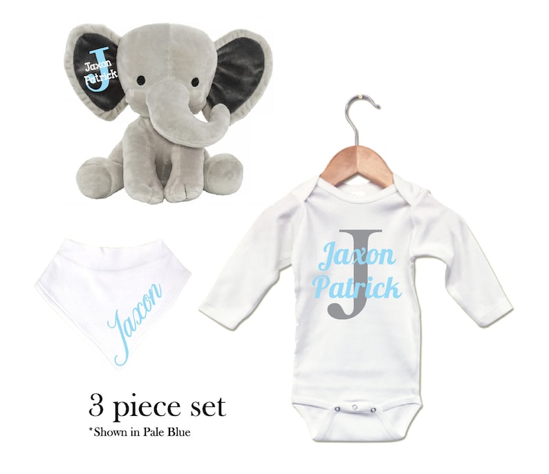 Puede incluir: Un conjunto de regalo para beb&eacute; de tres piezas con un juguete de elefante de peluche gris, un body blanco de manga larga y un babero blanco. El body y el babero est&aacute;n personalizados con el nombre "Jaxon Patrick" y la letra "J" en azul y gris. El juguete de elefante tiene la misma personalizaci&oacute;n en una oreja.
