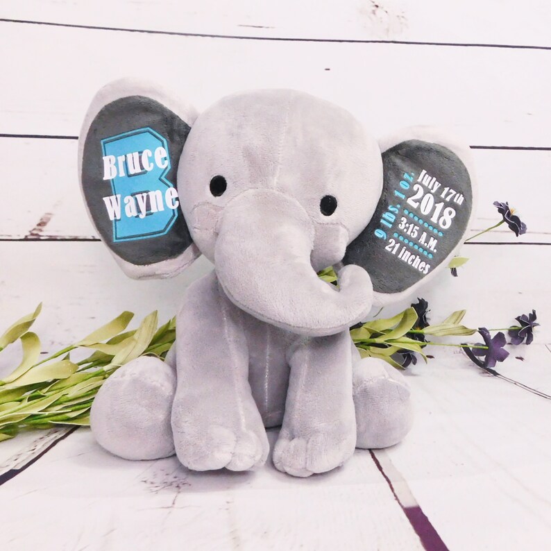 Puede incluir: Peluche de elefante gris de felpa con detalles bordados. Una oreja dice "Bruce Wayne" en texto azul y blanco. La otra oreja dice "9 lbs 1 oz, 17 de julio de 2018, 3:15 A.M., 21 pulgadas" en texto azul y blanco.