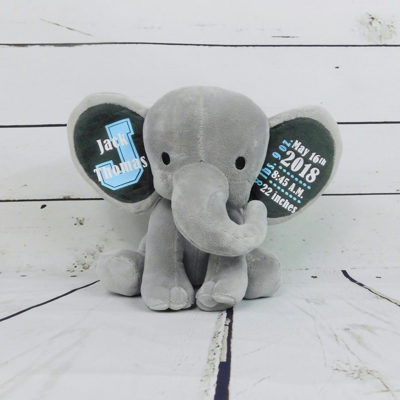 Puede incluir: Elefante de peluche gris con orejas azules y verdes. Las orejas est&aacute;n bordadas con el nombre "Jack Thomas", la fecha "16 de mayo de 2018", la hora "8:45 A.M." y el peso "7 libras 9 onzas" y la altura "22 pulgadas".