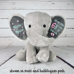 May include: Gray plush elephant with embroidered ears. One ear says "Kiera Louise" with pink hearts. The other ear says "09-22-2019 6 pounds 15 ounces 19" 3:48 A.M." with pink and teal embroidery.