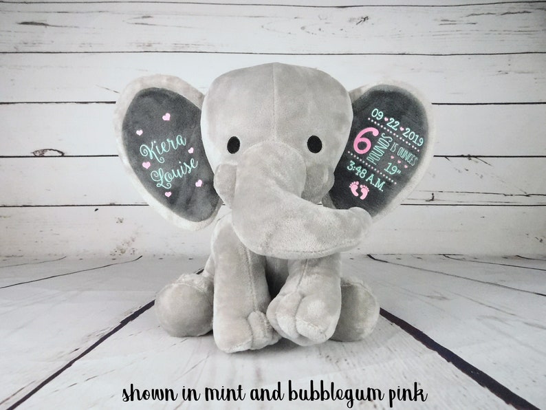 May include: Gray plush elephant with embroidered ears. One ear says "Kiera Louise" with pink hearts. The other ear says "09-22-2019 6 pounds 15 ounces 19" 3:48 A.M." with pink and teal embroidery.