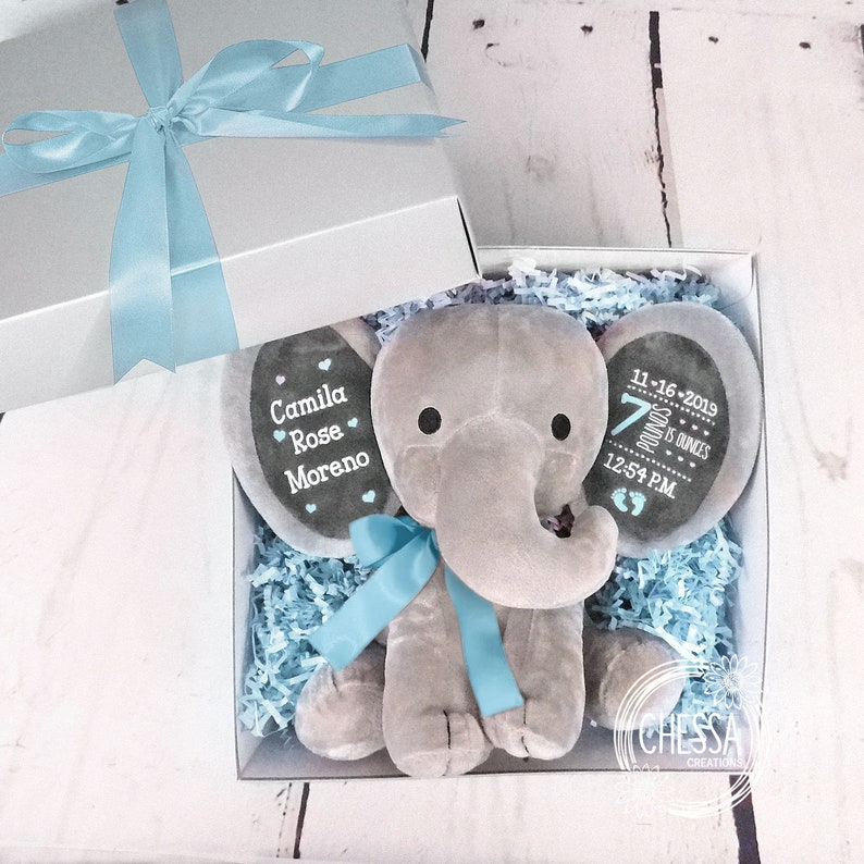 May include: A gray plush elephant stuffed animal in a gift box with blue tissue paper. The elephant has two black felt ears with personalized embroidery. One ear says "Camila Rose Moreno" and the other ear says "11-16-2019 7 pounds 15 ounces 12:54 PM".