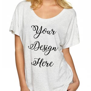 May include: A white, loose-fitting t-shirt with a scoop neck. The shirt has the text "Your Design Here" printed on the front in black cursive.