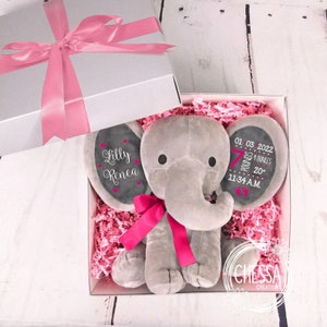 May include: A gray elephant plush toy with pink ribbon and a personalized message. The message reads "Lilly Renea" and "01 03 2022 7 pounds 20 ounces 11:34 A.M.". The toy is in a white gift box with pink tissue paper.