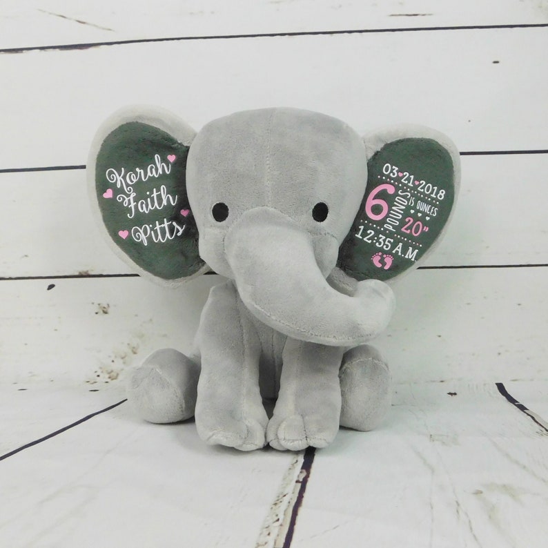May include: Gray plush elephant stuffed animal with embroidered details. The elephant's ears are personalized with the name "Korah Faith Pitts", the date "03-21-2018", the time "12:35 A.M.", and the baby's weight and length: "6 pounds 20 inches".