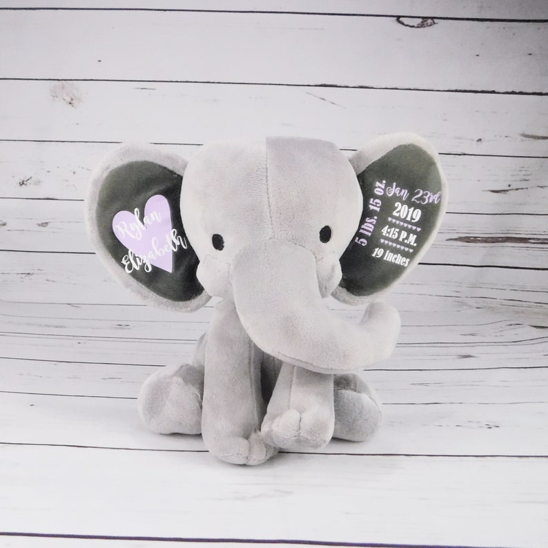 May include: Gray plush elephant with embroidered details. One ear has a pink heart with the names "Rylan Elizabeth" and the other ear has the date "Jan 23rd 2019", time "4:15 P.M." and measurements "5 lbs. 15 oz. 19 inches".