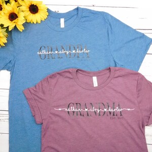 May include: Two t-shirts, one blue and one burgundy, with the word "GRANDPA" and "GRANDMA" printed on them. Below the words are names and the year "EST. 2012". Yellow sunflowers are in the background.