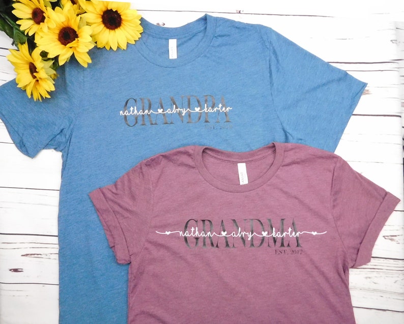 May include: Two t-shirts, one blue and one burgundy, with the word "GRANDPA" and "GRANDMA" printed on them. Below the words are names and the year "EST. 2012". Yellow sunflowers are in the background.