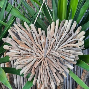 Peut inclure: Décoration murale en forme de cœur faite de bois flotté. Les morceaux de bois flotté, dans des tons de gris et de beige, sont disposés pour former un cœur texturé. Une corde naturelle est attachée pour l'accrocher. Le fond présente un feuillage vert.