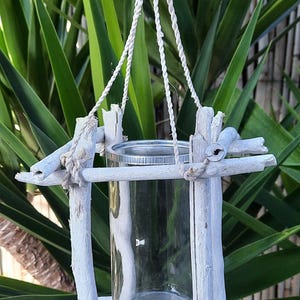 May include: A whitewashed driftwood planter with a glass cylinder hanging from a white rope. The planter is ideal for displaying small plants or flowers.