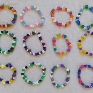 Könnte beinhalten: Zwölf bunte Perlenarmbänder mit sternförmigen Anhängern. Die Armbänder sind aus verschiedenen Farben von Perlen gefertigt, darunter rosa, blau, grün, gelb und lila.
