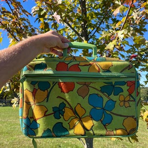 May include: A rectangular briefcase featuring a vibrant lime green base with a repeating floral pattern in shades of orange, yellow, and teal. The bag includes a matching lime green plastic handle, a zippered front pocket, and green piping.