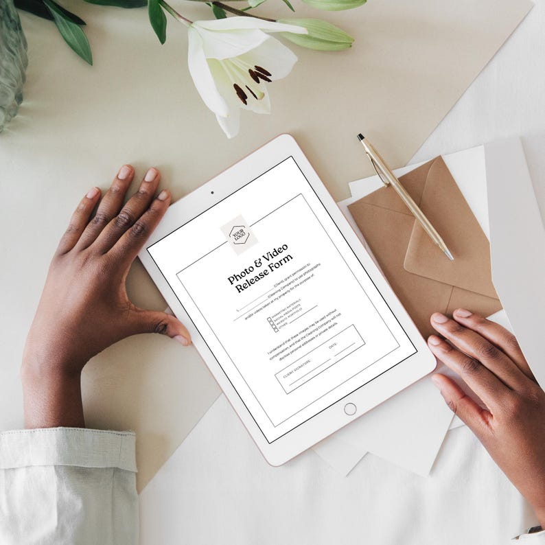 Pu&ograve; includere: Un tablet bianco che mostra un "Photo & Video Release Form" con un logo in alto. Il tablet &egrave; tenuto in mano, con una penna e una busta nelle vicinanze. Gigli bianchi e cancelleria sullo sfondo.