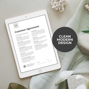K&ouml;nnte beinhalten: Ein digitales Tablet, das ein "Customer Agreement"-Dokument mit einem Logo anzeigt. Das Dokument ist in schwarzem Text auf wei&szlig;em Hintergrund. Ein dunkelgrauer Kreis mit dem Text "CLEAN MODERN DESIGN" befindet sich auf der rechten Seite. Das Tablet liegt auf einem hellgr&uuml;nen Stoff.