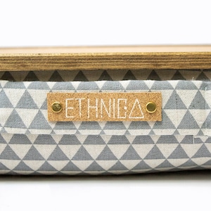 Pu&ograve; includere: Un contenitore di stoccaggio con motivo geometrico grigio e bianco con un top in legno e un'etichetta in sughero che recita "ETHNICA".