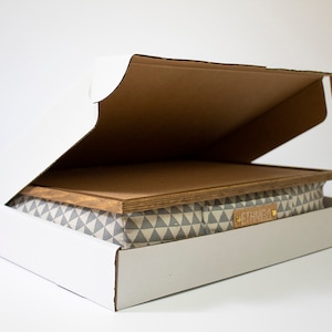 Pu&ograve; includere: Una scatola di cartone bianca con il lembo superiore aperto, che rivela una scatola di stoffa con motivo grigio e bianco con un coperchio in legno. La scatola di stoffa ha un'etichetta in pelle marrone con la parola "ETERNAL" stampata su di essa.