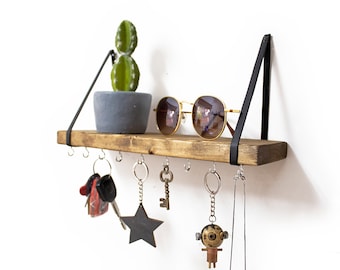 May include: A wooden shelf with black metal brackets, featuring a small potted cactus, sunglasses, and a variety of keychains, including a star, a key, and a small figurine.
