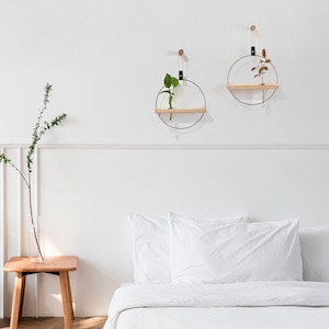 May include: Two circular wall shelves with gold metal frames and wooden shelves. Each shelf has a small plant in a glass vase.