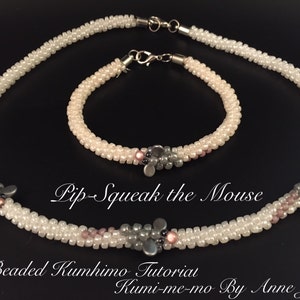 May include: A white beaded necklace and bracelet set with gray and pink accents. The set is called "Pip-Squeak the Mouse" and is a beaded kumhimo tutorial by Anne Jones.