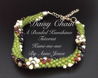 Puede incluir: Un brazalete de cuentas verde, blanco y plateado con un diseño de cadena de margaritas. El brazalete está hecho con la técnica kumihimo. El texto "Daisy Chain A Beaded Kumihimo Tutorial Kumi-me-mo By Anne Jones" está escrito en la imagen.