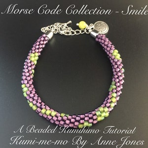 Peut inclure: Un bracelet en perles violet et vert avec un fermoir argenté et un charme smiley. Le bracelet est réalisé à l'aide de la technique du kumihimo. Le texte "Morse Code Collection - Smile" et "A Beaded Kumihimo Tutorial Kumi-me-mo By Anne Jones" est visible sur l'image.