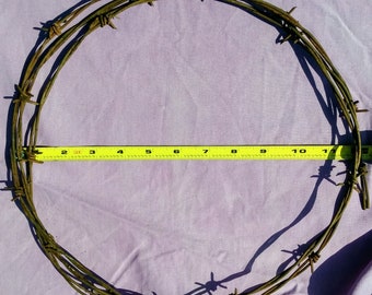 May include: A rusty, brown, barbed wire wreath measuring 10 inches in diameter.