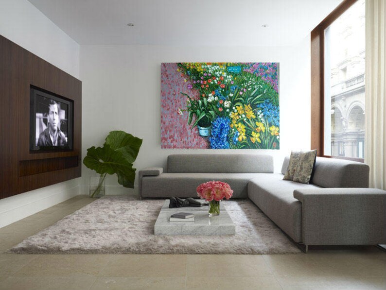 May include: A gray sectional sofa with a floral painting above it. The sofa is in a modern living room with a large window and a flat screen TV on the wall.