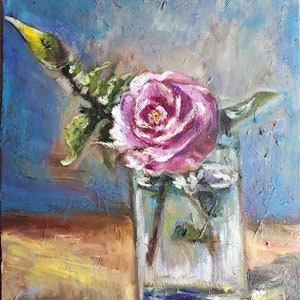 May include: A single pink rose with a yellow bud is in a clear glass vase on a wooden table. The background is a textured blue wall.