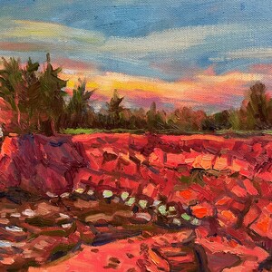 Puede incluir: Una pintura de una costa rocosa con un cielo de puesta de sol vibrante. Las rocas son de un rojo intenso y el cielo es una mezcla de rosa, naranja y amarillo. Hay &aacute;rboles en el fondo y el agua es de un azul profundo.