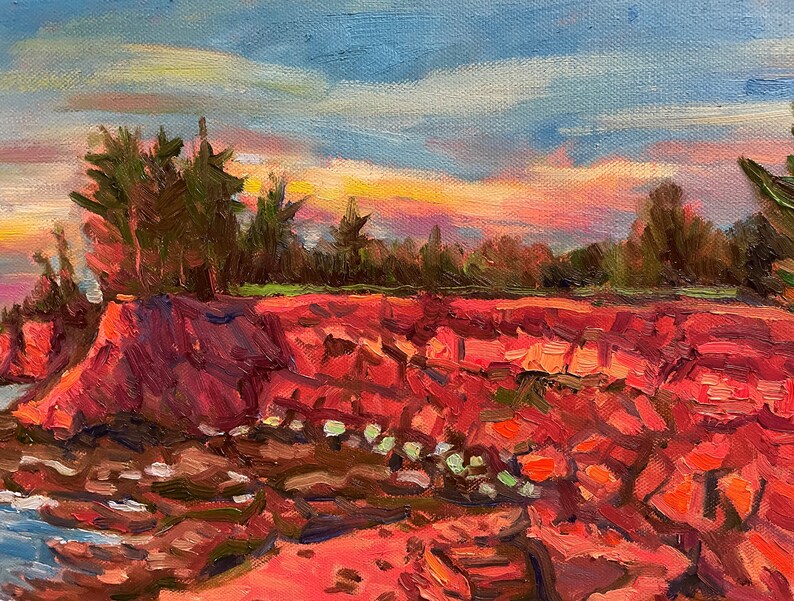 Puede incluir: Una pintura de una costa rocosa con un cielo de puesta de sol vibrante. Las rocas son de un rojo intenso y el cielo es una mezcla de rosa, naranja y amarillo. Hay &aacute;rboles en el fondo y el agua es de un azul profundo.