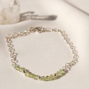 May include: A delicate silver chain bracelet with a row of light green gemstone beads.