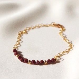 Peut inclure: Un bracelet en chaîne dorée avec une rangée de petites perles de pierres précieuses rouge foncé.